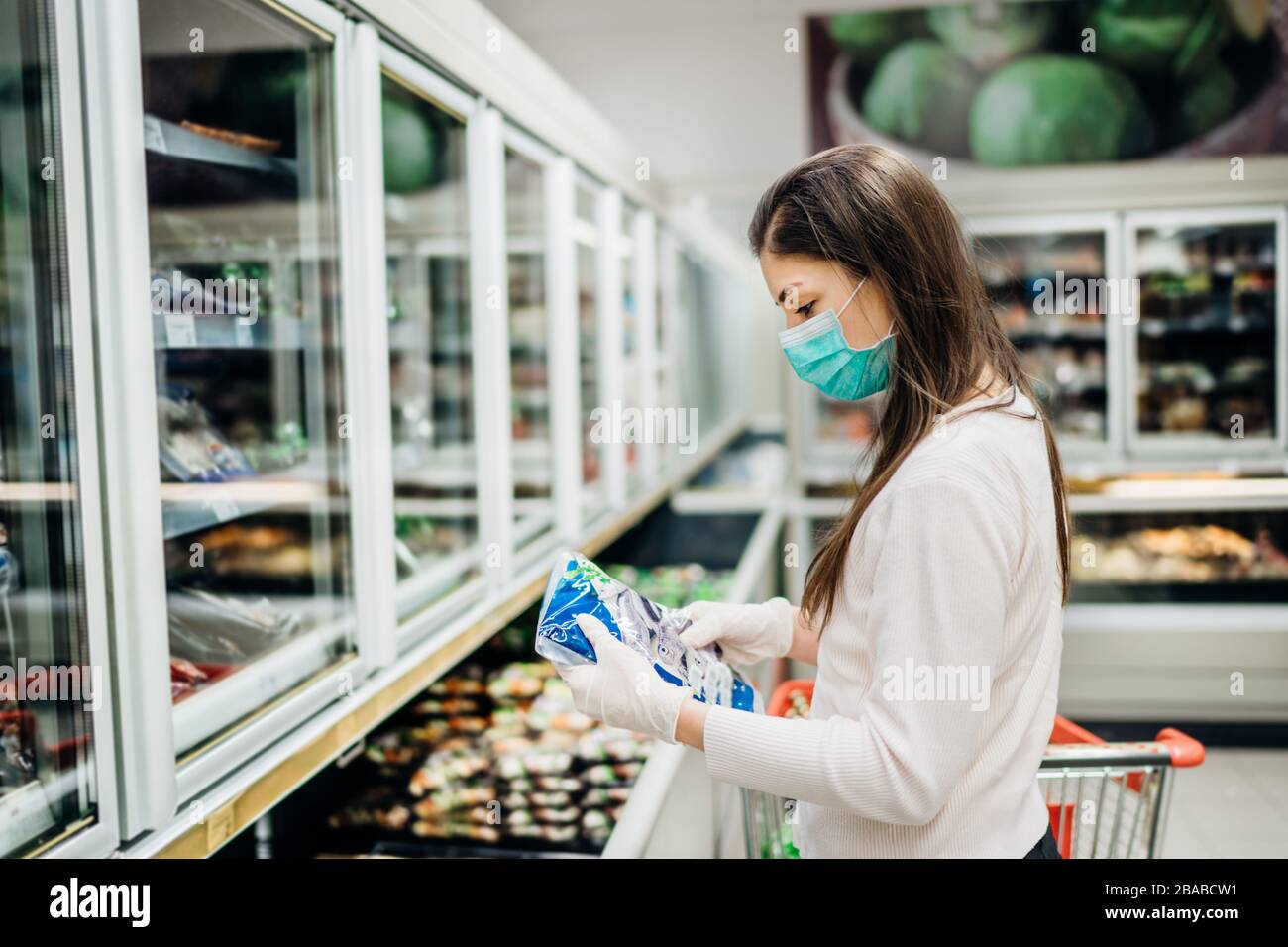 Femme portant un masque de visage achetant dans un supermarché.Panic shopping pendant Coronavirus covid-19 pandémique.Budget acheter dans un magasin d'approvisionnement.Acheter congélateur intelligent Banque D'Images