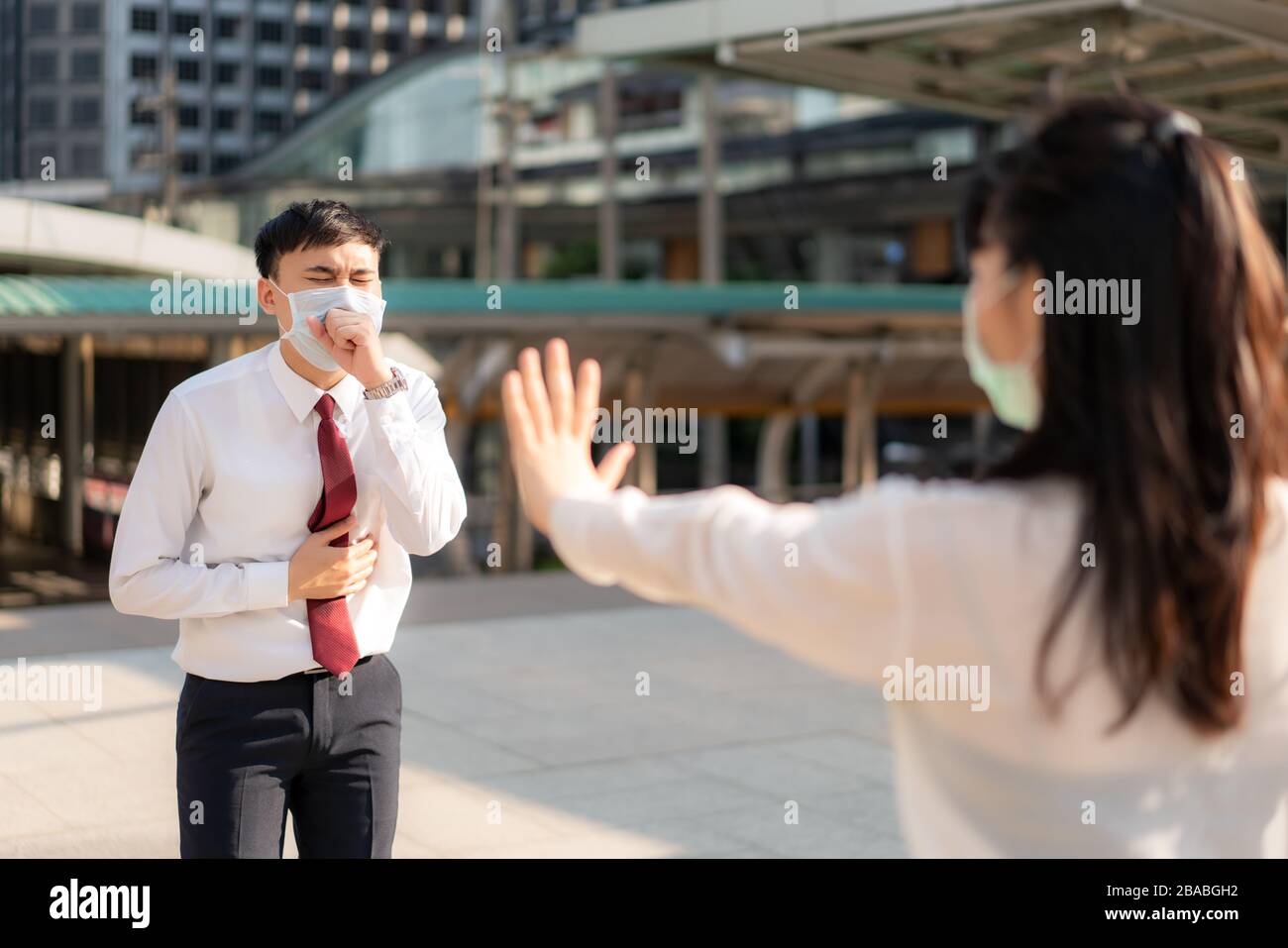 Un homme d'affaires asiatique malade tousse avec masque et une femme d'affaires stop signe lui main pour garder la distance de protection contre les virus COVID-19 et les personnes social distancing Banque D'Images