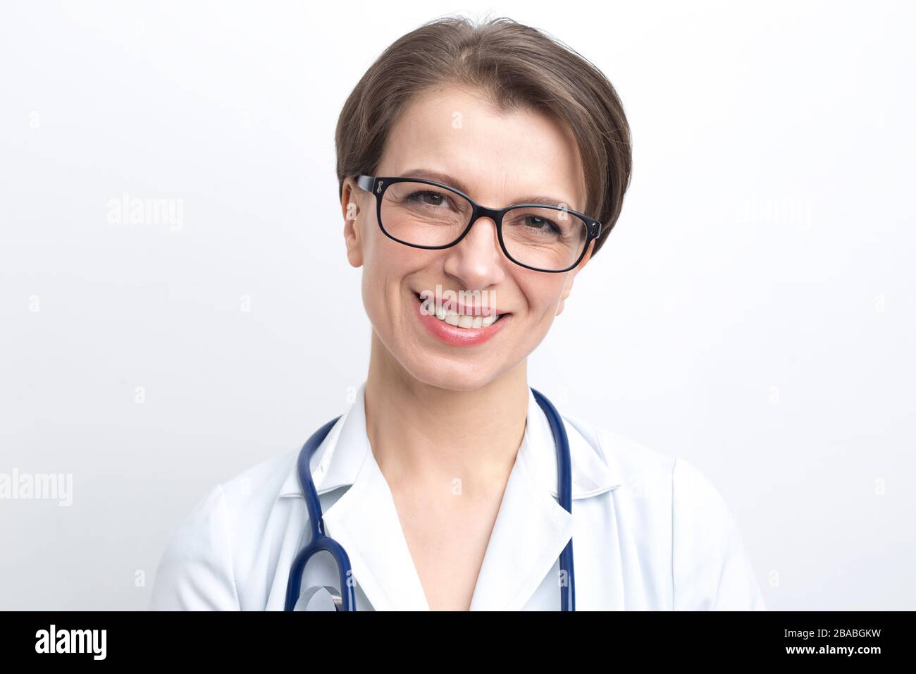 Portrait d'une femme souriante en blouse de laboratoire avec un stéthoscope sur fond blanc. Banque D'Images