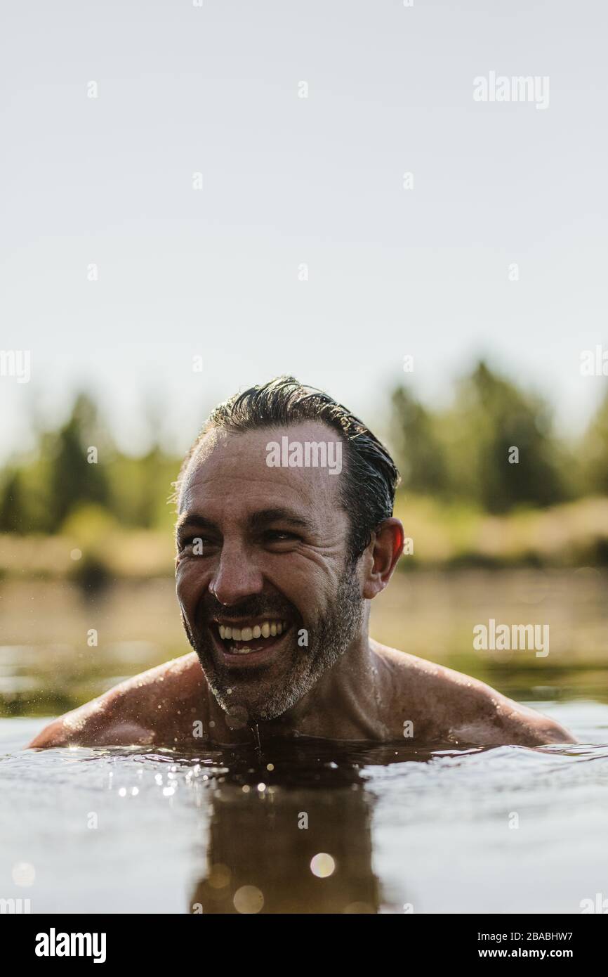 Homme mûr souriant nageant dans un lac. Visage d'un homme adulte moyen au-dessus de la surface de l'eau regardant loin et souriant. Banque D'Images Homme mûr souriant nageant dans un lac. Visage d'un homme adulte moyen au-dessus de la surface de l'eau regardant loin et souriant. Banque D'Images