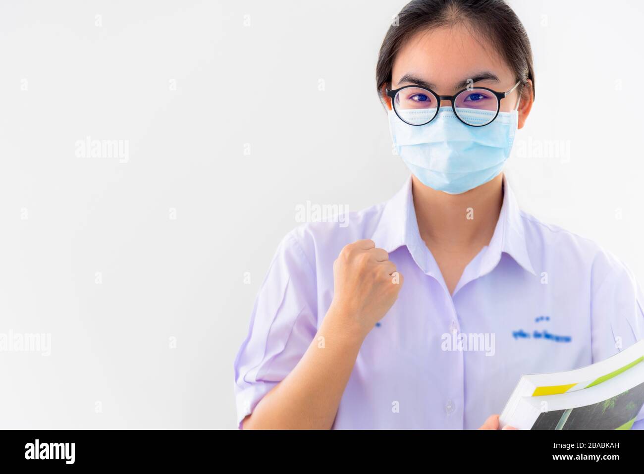 La jeune femme asiatique étudiante porte un masque pour protéger la propagation du Coronavirus, une fille thaïlandaise pour encourager le symbole du poing à se battre et forte sur fond blanc Banque D'Images