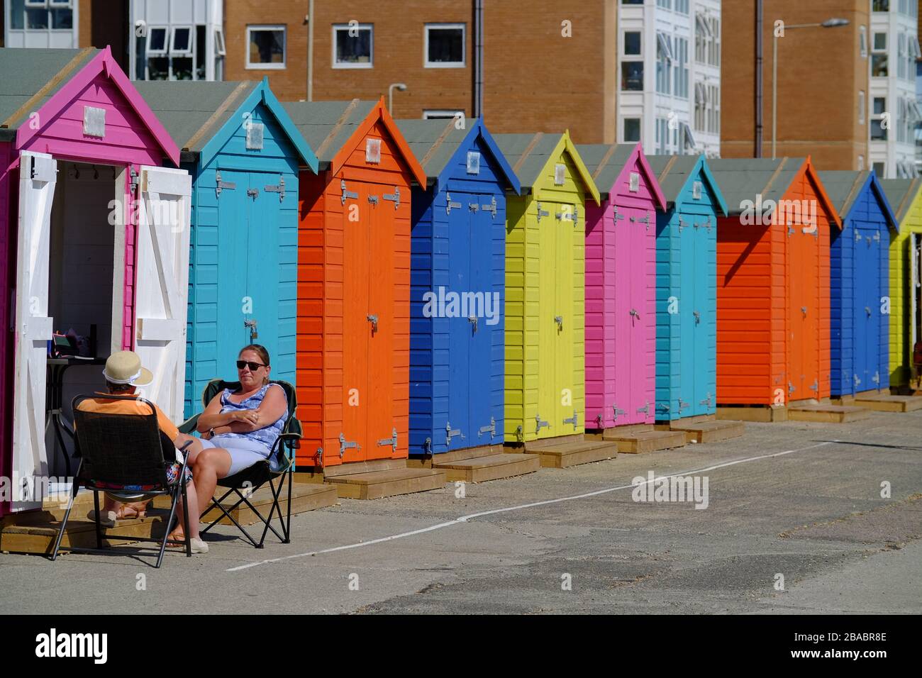 Couple détente par des huttes de plage colorées, Seaford, Royaume-Uni Banque D'Images