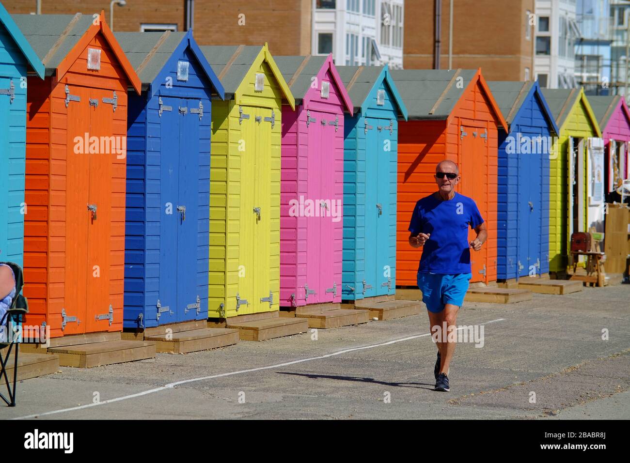 Homme âgé jogging le long d'un front de mer par des cabanes de plage colorées. Seaford, Royaume-Uni Banque D'Images