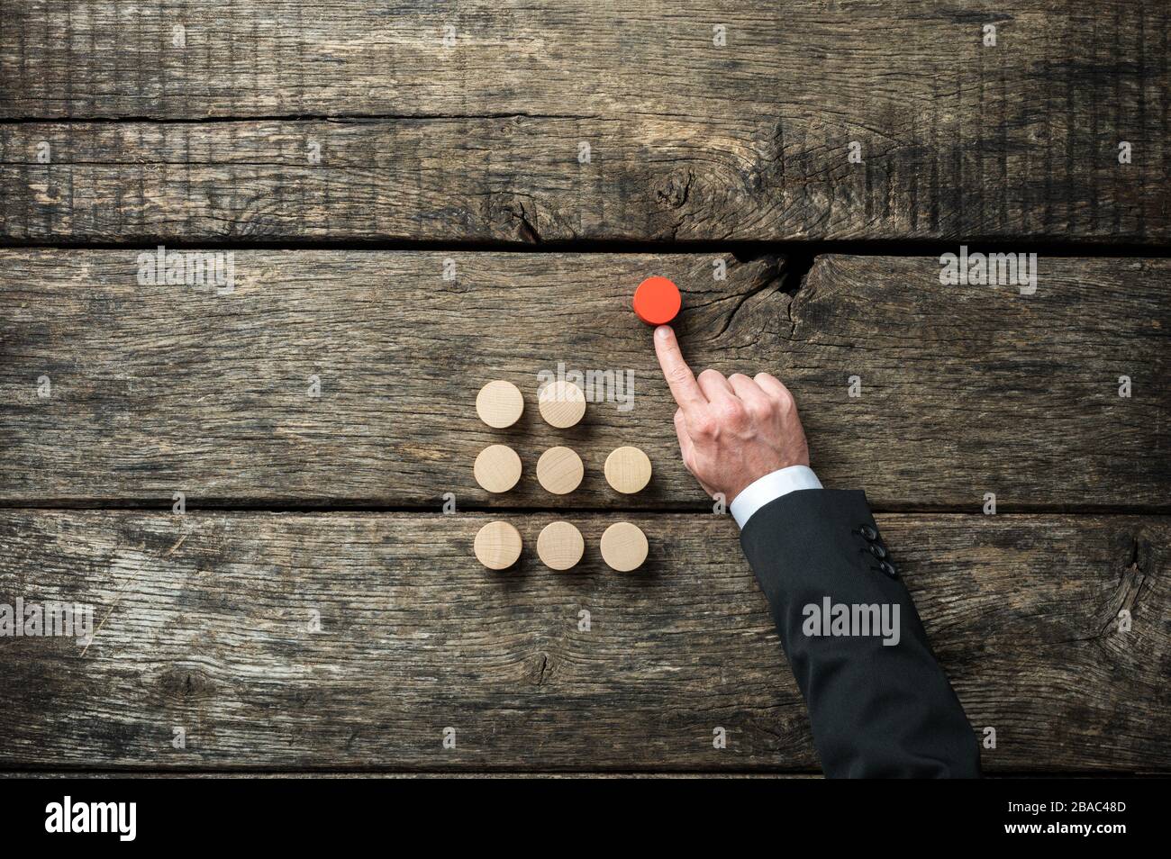 Main d'un homme d'affaires poussant rouge en bois coupé cercle hors de la corneille d'autres dans une image conceptuelle de l'auto-initiative et de la détermination. Banque D'Images