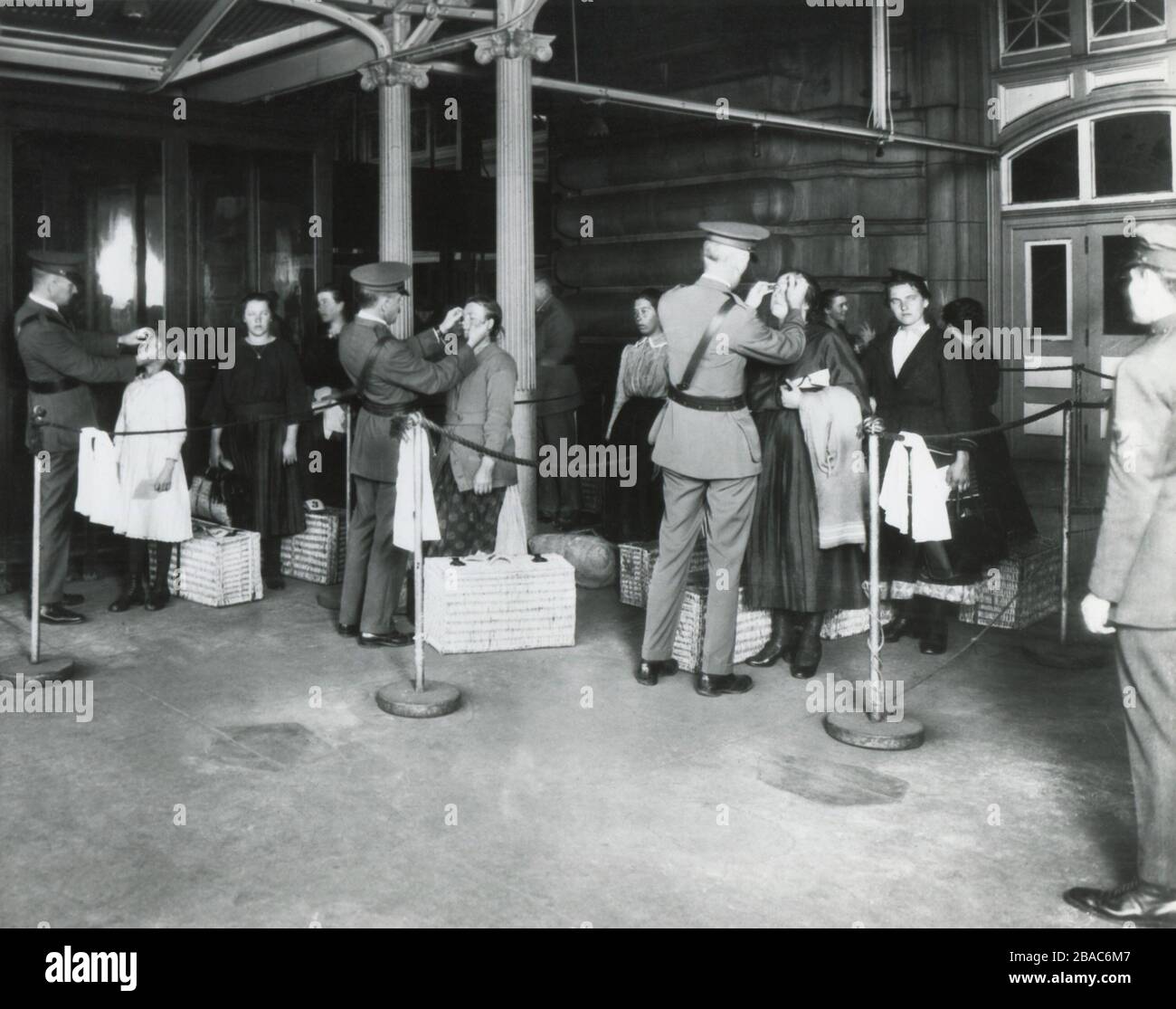 Inspection des immigrants arrivés par la fonction de santé publique à Ellis Island, c. 1910. L'inspecteur a levé la paupière avec un boutonnière, examinant les maladies des yeux, en particulier le trachome (BSLOC_2018_1_19) Banque D'Images
