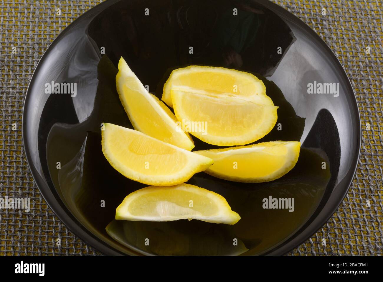 Tranches de quartiers frais de fruits de citron cru dans un bol noir sur la table Banque D'Images