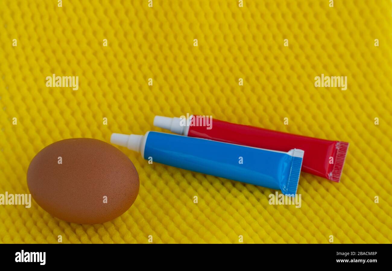 Colorant pour oeufs de Pâques. Peinture dans des tubes et un oeuf de poulet sur un fond jaune vif Banque D'Images