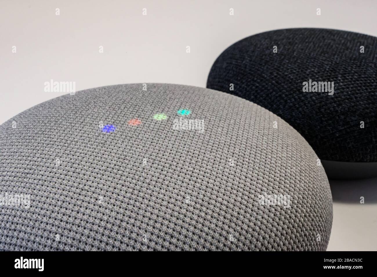 Une vue rapprochée d'une mini-enceinte intelligente Google Nest montre ses lumières colorées activées, avec une autre Mini Nest assise derrière elle. Banque D'Images
