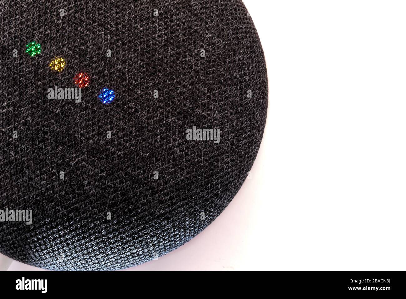 Une mini-enceinte intelligente Google Nest grise foncé avec Google Assistant est posée sur une surface blanche. Ses lumières montrent les couleurs de la marque et du logo de Google. Banque D'Images