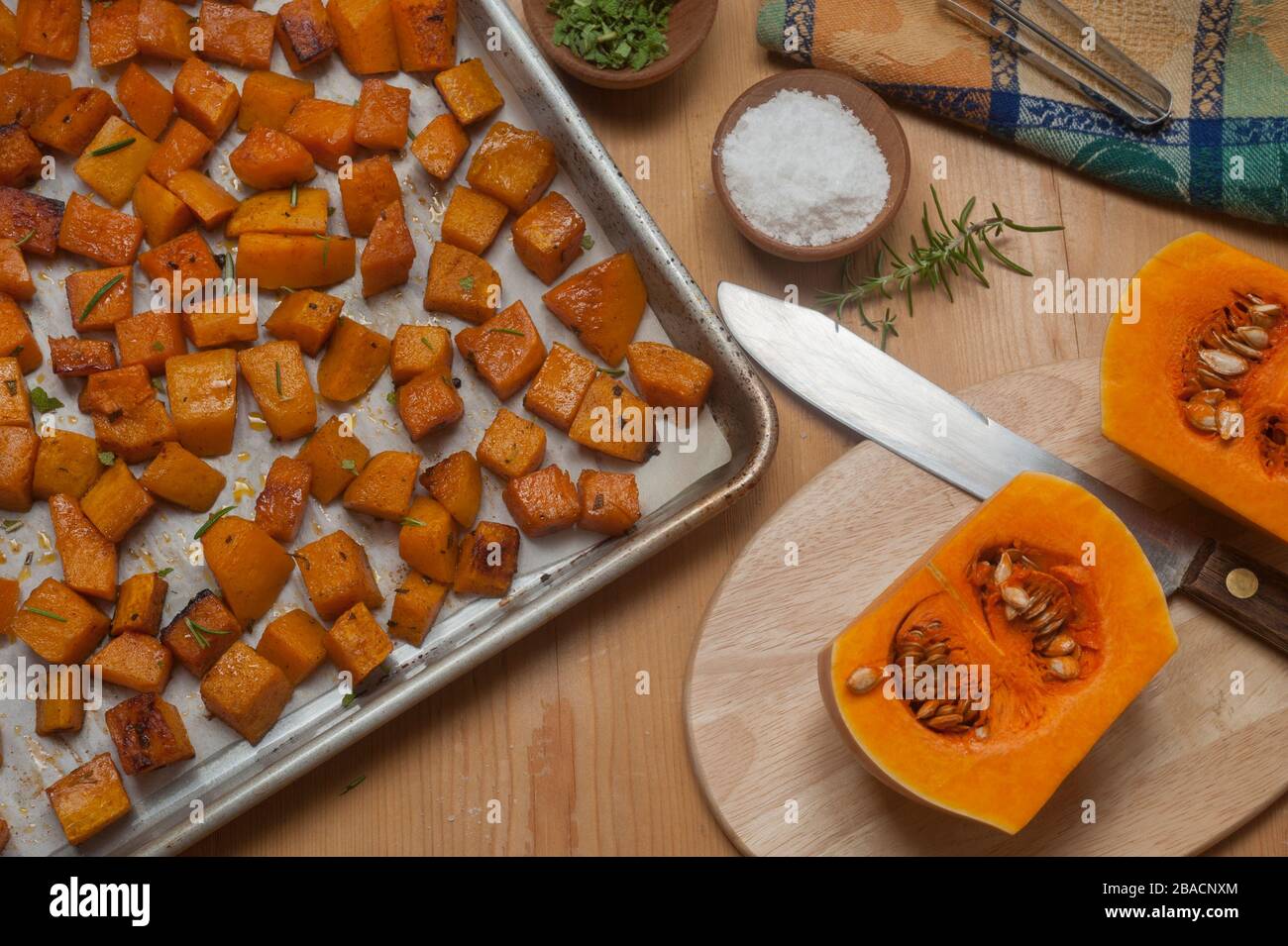 Cubes de courge musquée rôtie dans la poêle et moitiés brutes sur la planche à découper avec des herbes et des épices dans de petits bols en bois. Banque D'Images