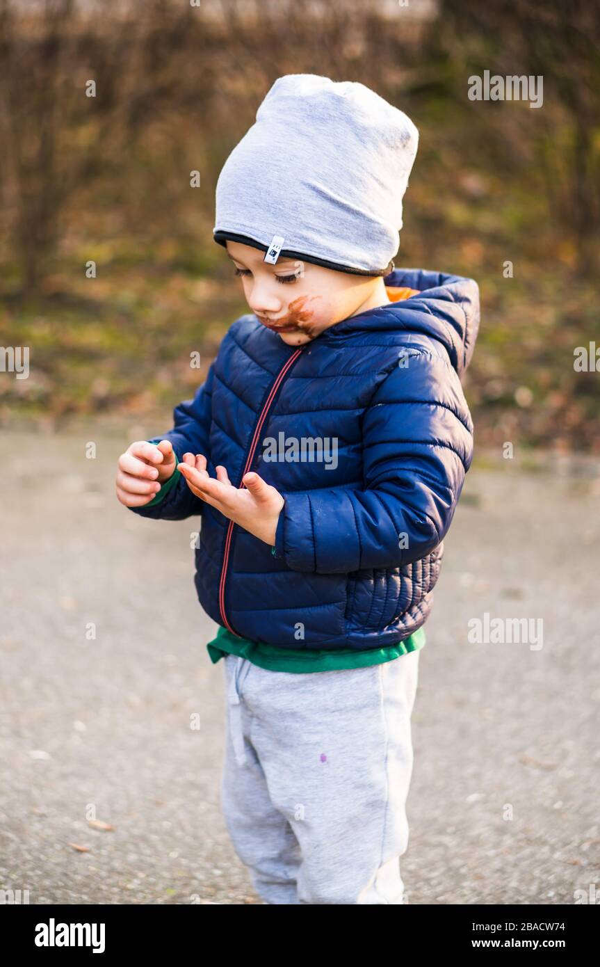 POZNAN, POLOGNE - 16 mars 2020: Petit garçon de deux ans avec bouche sale regardant ses mains dans un parc. Banque D'Images