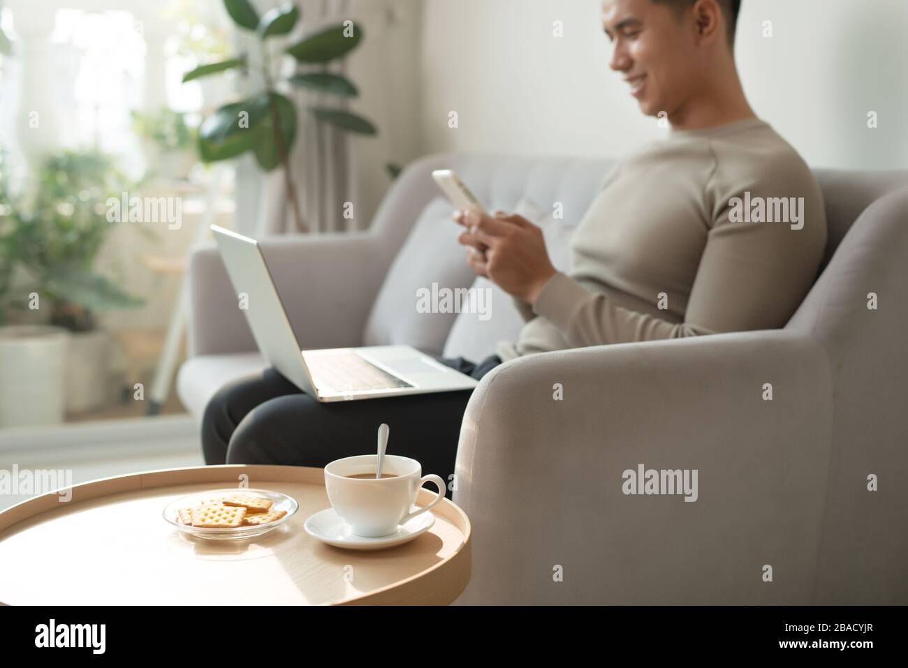Homme utilisant un smartphone et un ordinateur portable sur un canapé Banque D'Images