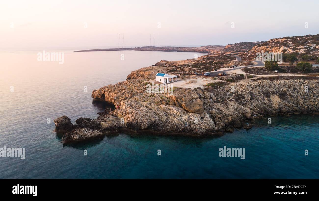 Vue aérienne sur le coucher du soleil de la côte et site touristique de la  chapelle blanche délavée Agioi Anargyroi, à Cavo Greco Protaras, Famagusta,  Chypre d'en haut. Vie des yeux d'oiseaux