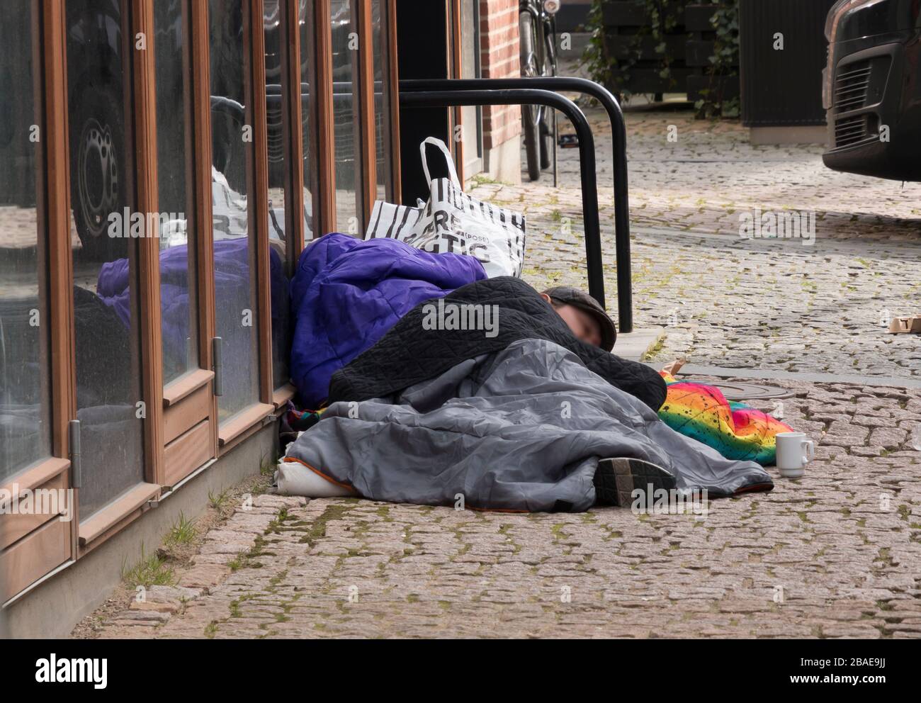 Aarhus, Danemark - 24 mars 2020: Un homme sans abri dormait sur un lit skt. Knuds Torv à Aarhus, c'est une journée froide et la main est sur les pierres dures Banque D'Images