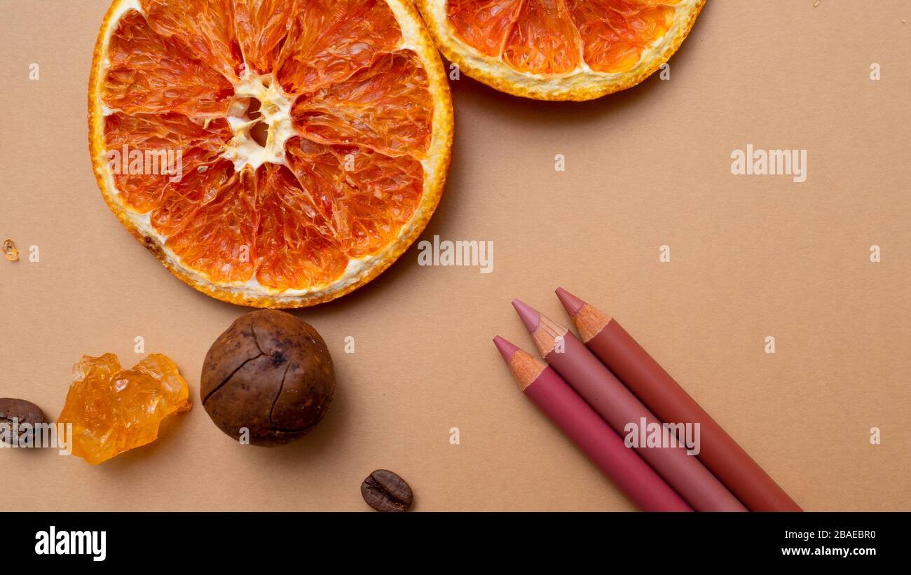 Cosmétiques pour le maquillage naturel, crayons à lèvres. Fond chaud avec café à noix et fruits secs. Banque D'Images