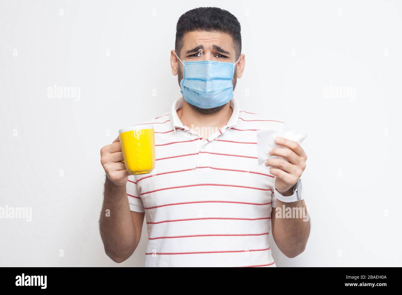 Malheureuse inquiétude homme malade avec masque médical chirurgical debout et tenant la tasse jaune avec le tissu blanc, boire le thé chaud, a la grippe, malade ou coronavirus. Indo Banque D'Images