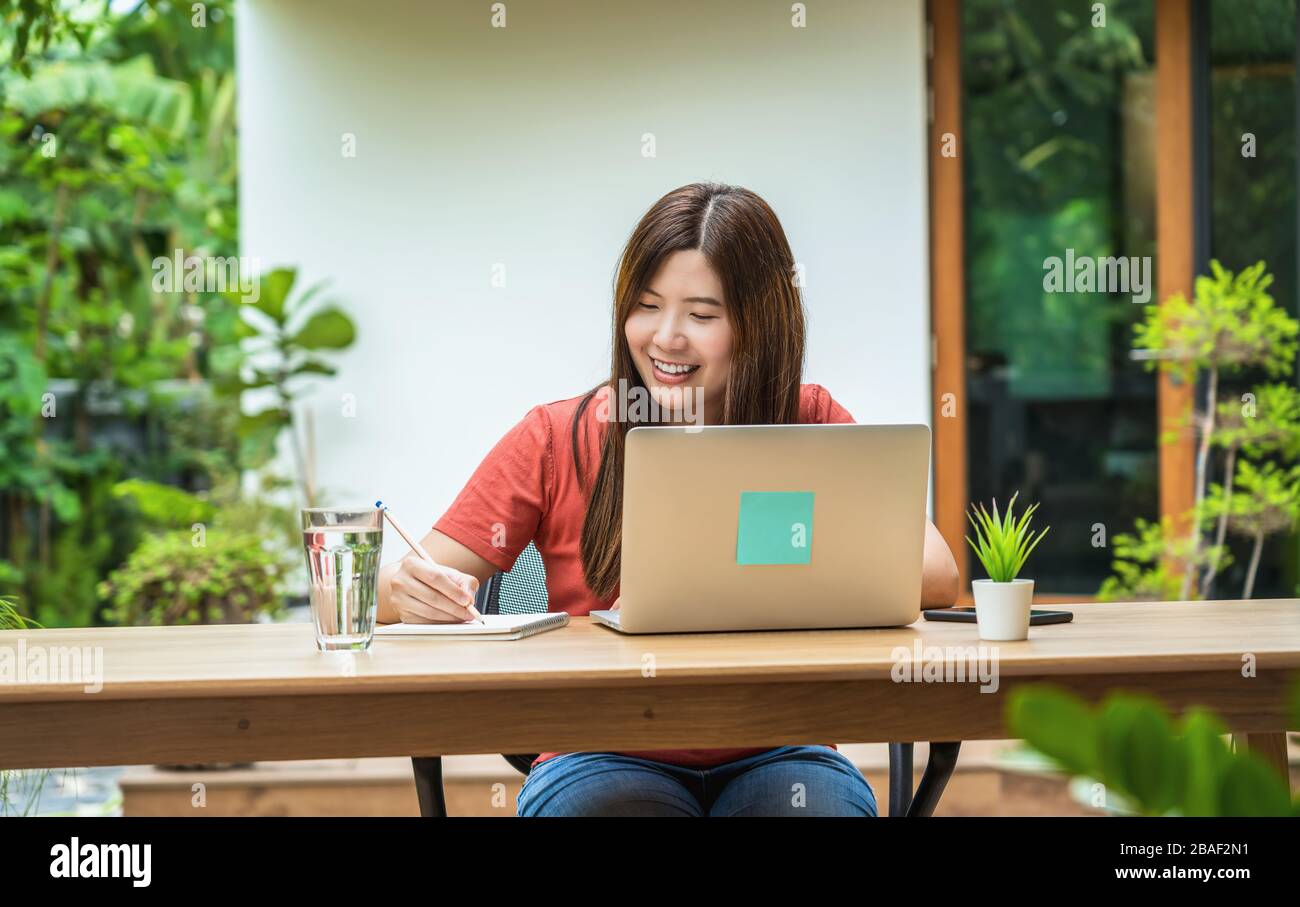 Femme d'affaires asiatique utilisant un ordinateur portable de technologie et un carnet d'écriture pour travailler de la maison en plein air maison et jardin, startups et propriétaire d'entreprise, socia Banque D'Images