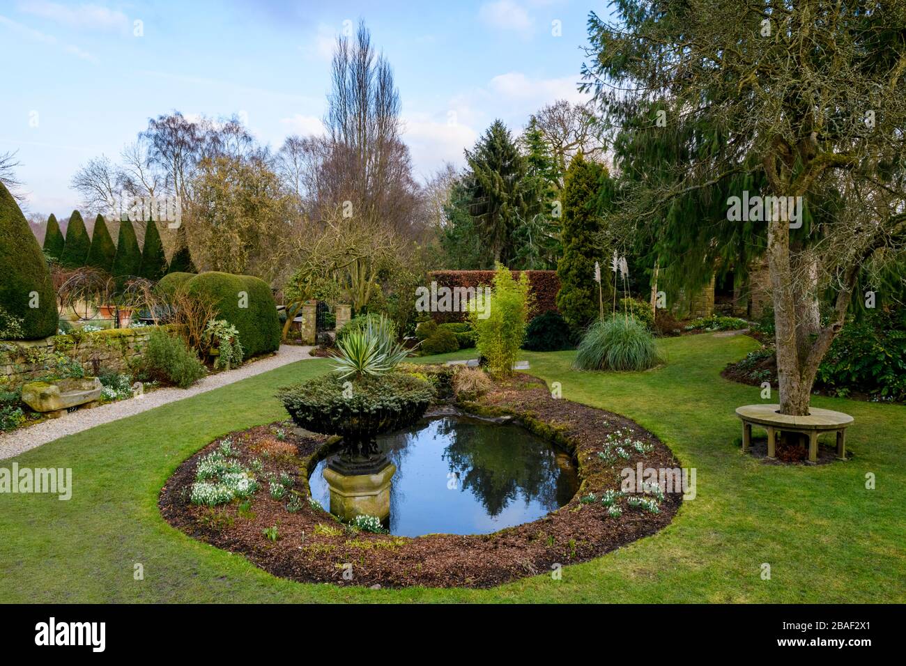 Jardin de campagne (réflexions d'eau d'étang, siège circulaire, urne décorative, chemin de gravier, pieuvre, pelouse, arbres matures) - York Gate Garden, Leeds UK. Banque D'Images
