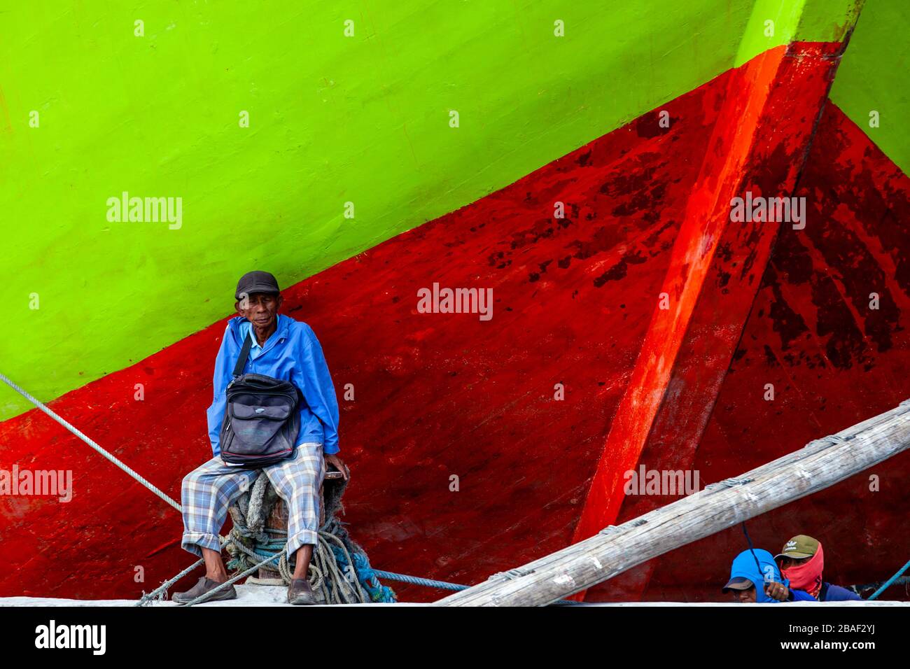 Un homme local assis par un bateau à voile traditionnel en bois (Pinisi) au vieux port de Sunda Kelapa, Jakarta, Indonésie. Banque D'Images