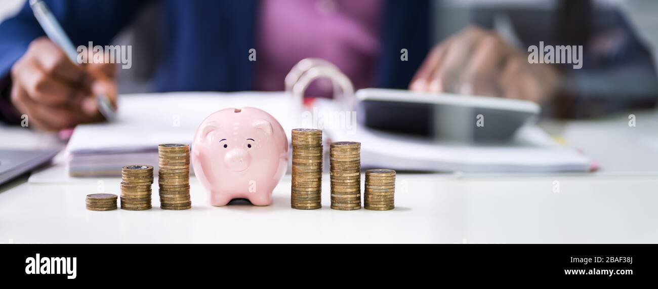 Close-up of Businessman Calcul Loi Avec Piggybank et empilés pièces sur Desk In Office Banque D'Images