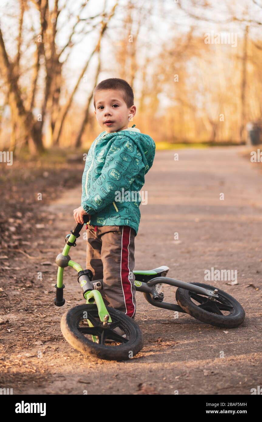 POZNAN, POLOGNE - 16 mars 2020: Petit jeune garçon debout par un vélo de course tombé sur un sentier dans un parc. Banque D'Images