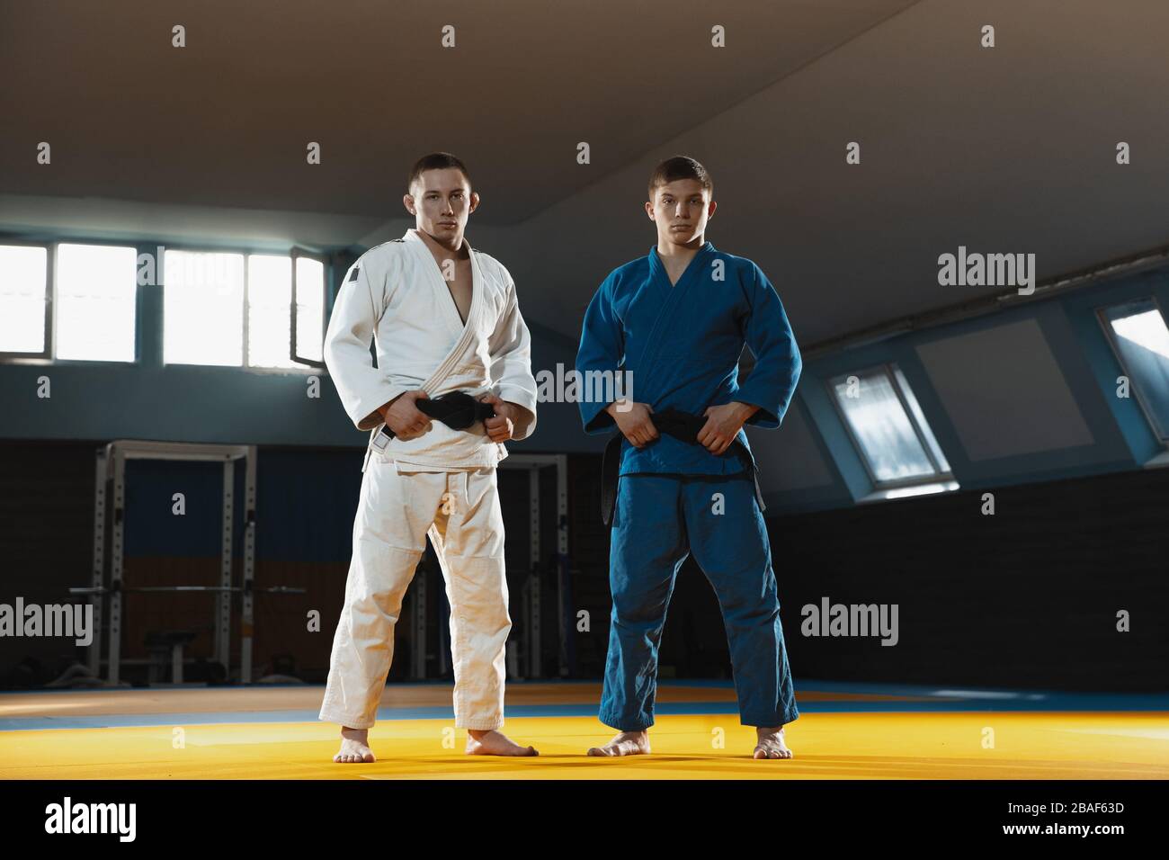 Deux jeunes combattants caucasiens judo en kimono blanc et bleu avec ceintures noires posant confiance dans la salle de gym, forte et saine. Pratiquer des habiletés de combat en arts martiaux. Surmonter, atteindre l'objectif. Banque D'Images