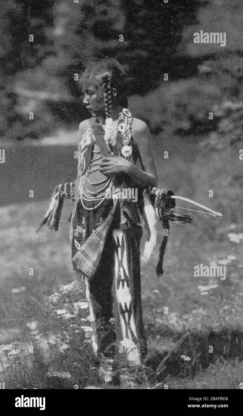 American Indian / Native American boy pose avec un arc et des flèches dans une gaine ou un quiver sur son dos, vers 1907. Il porte une belle collection de vêtements magnifiquement conçus et ornés de perles, y compris des leggings, un tissu de breechwth, des mocassins (non visibles) et des cordes autour de son cou. Il ne semble pas heureux. En fait, comme c'était assez fréquent ces jours-là, le photographe blanc a eu le garçon mis sur tous les vêtements authentiques mais pas de tous les jours seulement à poser, de sorte que le photographe pourrait vendre une image indienne romantique aux touristes. Pour voir mes autres images anciennes, recherchez: Prestor vintage West Banque D'Images