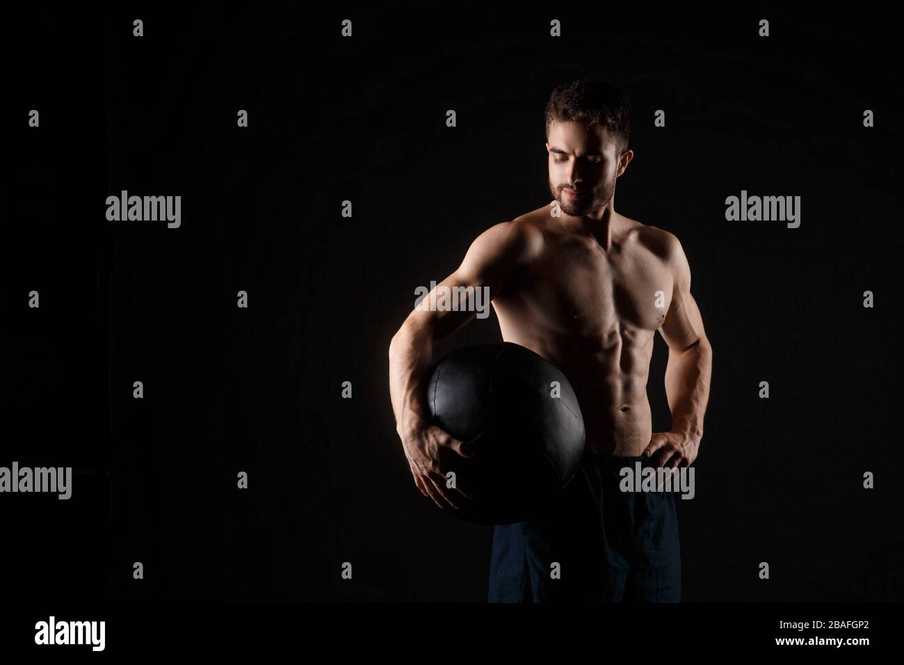 un athlète masculin en bonne forme physique sur un fond noir avec un medball dans ses mains. Banque D'Images