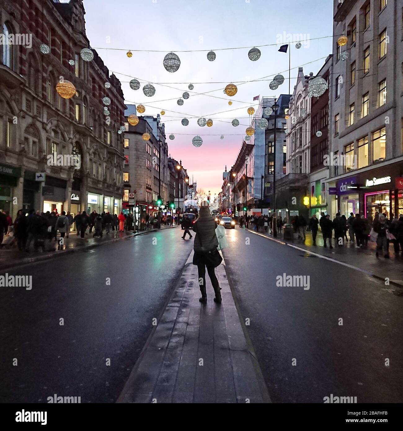 Oxford Street, Londres. Vue sur le quartier commerçant animé de Londres avec un acheteur anonyme admirant les lumières de Noël et le coucher du soleil. Banque D'Images
