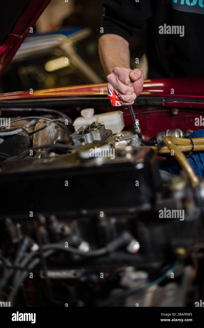 Main d'homme blanc avec des outils travaillant sur le moteur d'une voiture britannique avec capot ouvert avec un bandaid Union Jack sur sa main. Banque D'Images