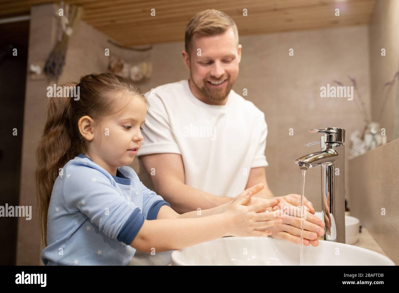 Jolie fille se lavant les mains sous l'eau et l'évier tandis que son père se tient près de pendant l'hygiène du matin dans la salle de bains Banque D'Images