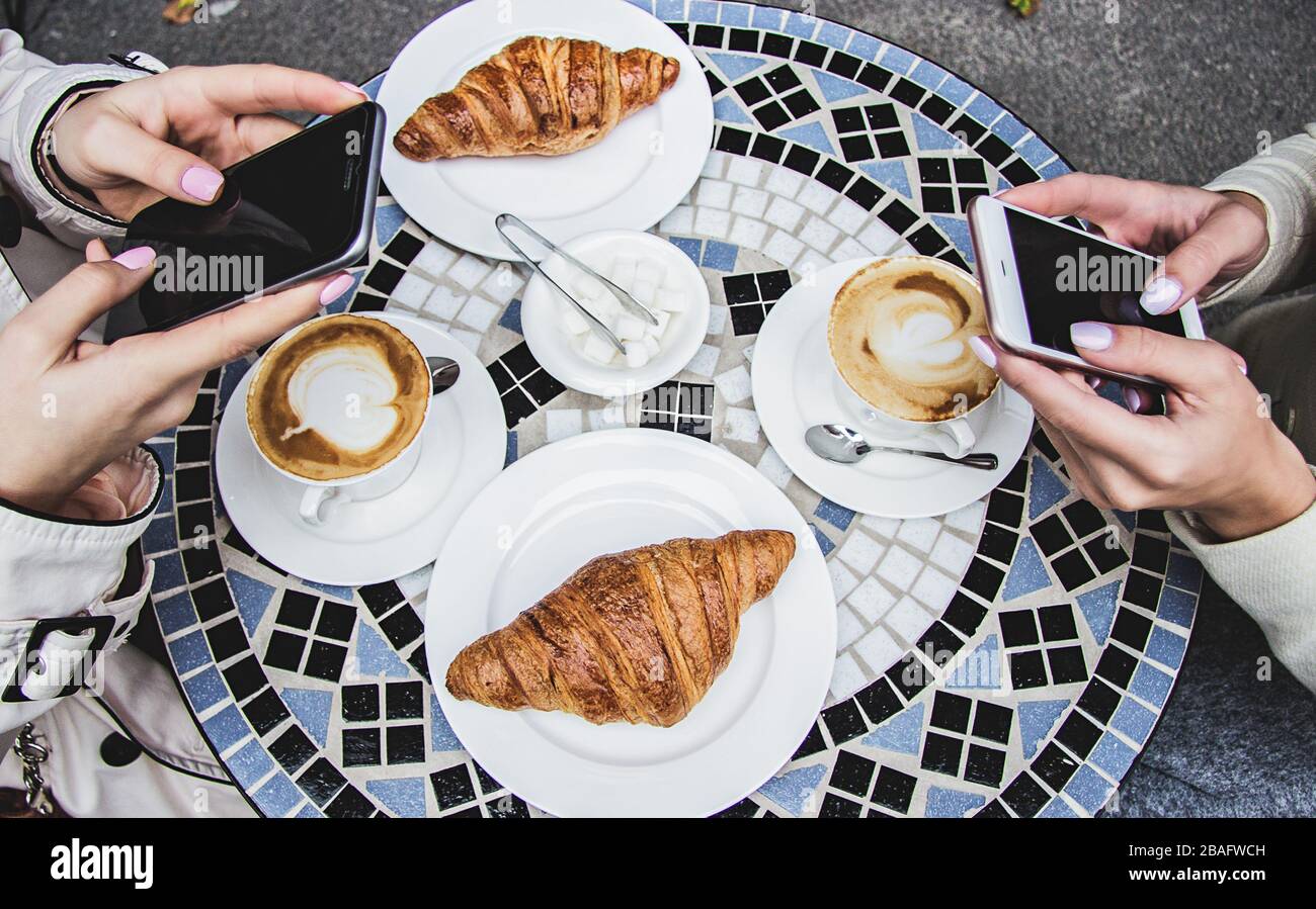 Vue de dessus des mains des femmes utilisant des smartphones pendant la consommation de café. Deux femmes ayant un frein à café dans le café français. Filles amis boire du café en français Banque D'Images