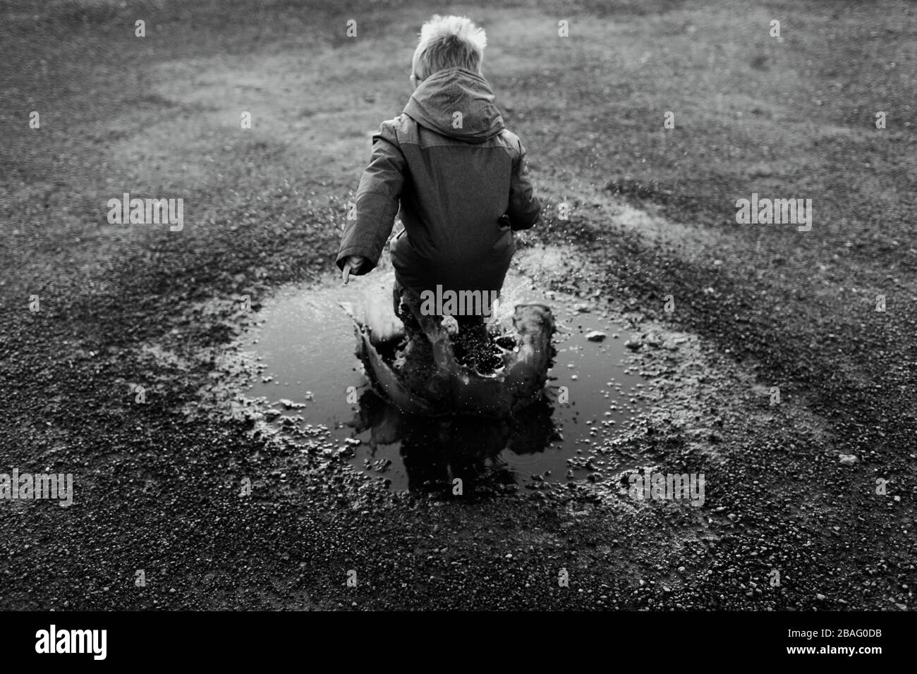 Un petit garçon sautant dans une flaque et créant un énorme splash en noir et blanc (B&W) Banque D'Images