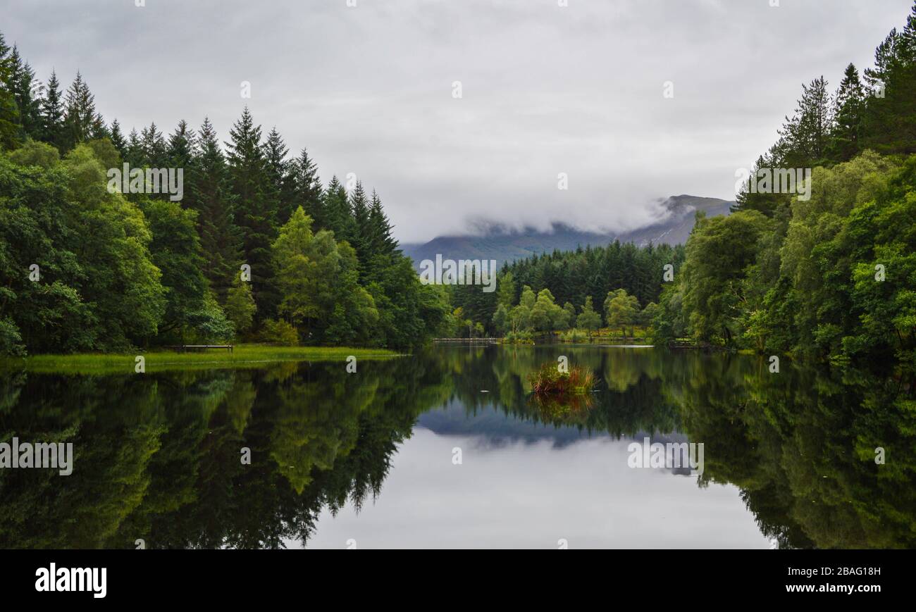 Paysage et réflexions de lac entouré d'une forêt à Glencoe Lochan en journée nuageux, dans les Highlands écossais, en Écosse. Banque D'Images