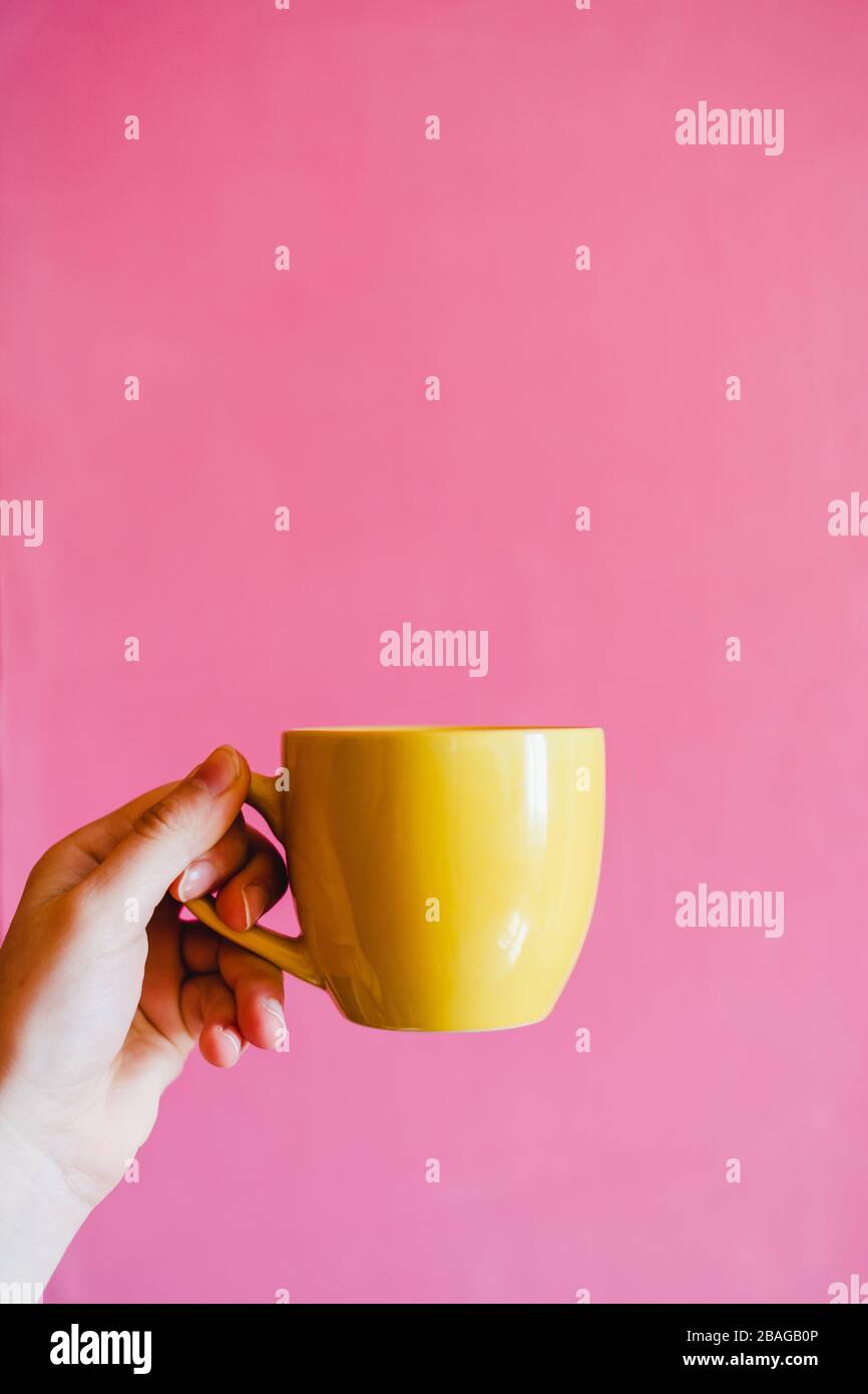 Tasse jaune dans la main avec fond de mur rose vif dans la lumière vive Banque D'Images