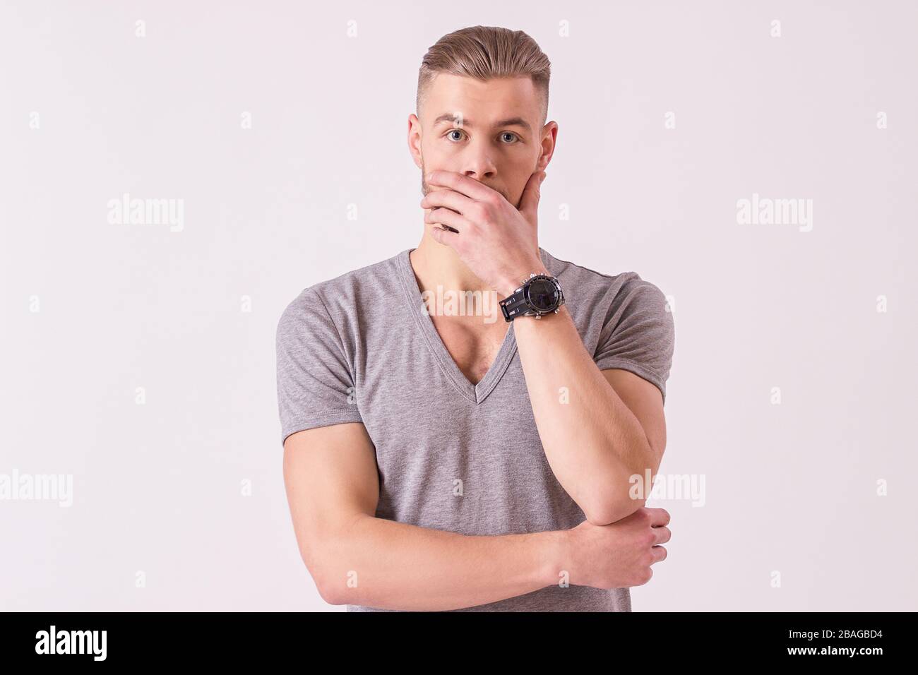 Portrait de jeune homme surpris faisant face et couvrant la bouche avec la main tout en étant isolé sur fond blanc. Hipster barbu choqué regardant l'appareil photo Banque D'Images