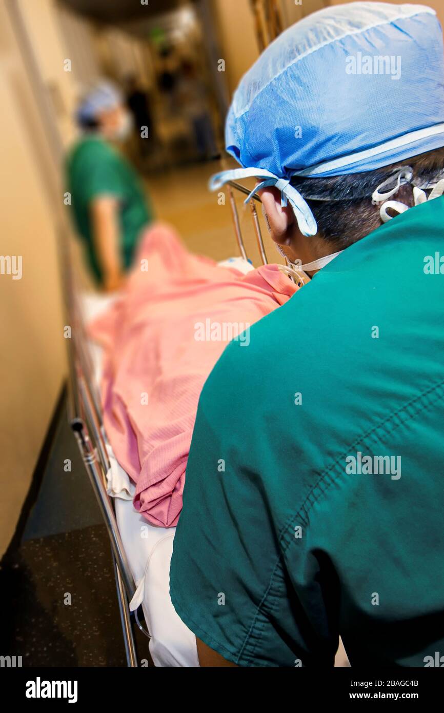 Image avec la perspective de suivre les professionnels médicaux dans les gommages verts poussant un gurney dans le couloir de l'hôpital avec le patient couvert dans la couverture rose Banque D'Images