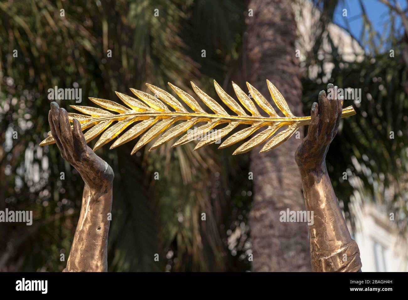 Gros plan sur la main d'une statue de bronze tenant une branche de palmiers dorés. Banque D'Images