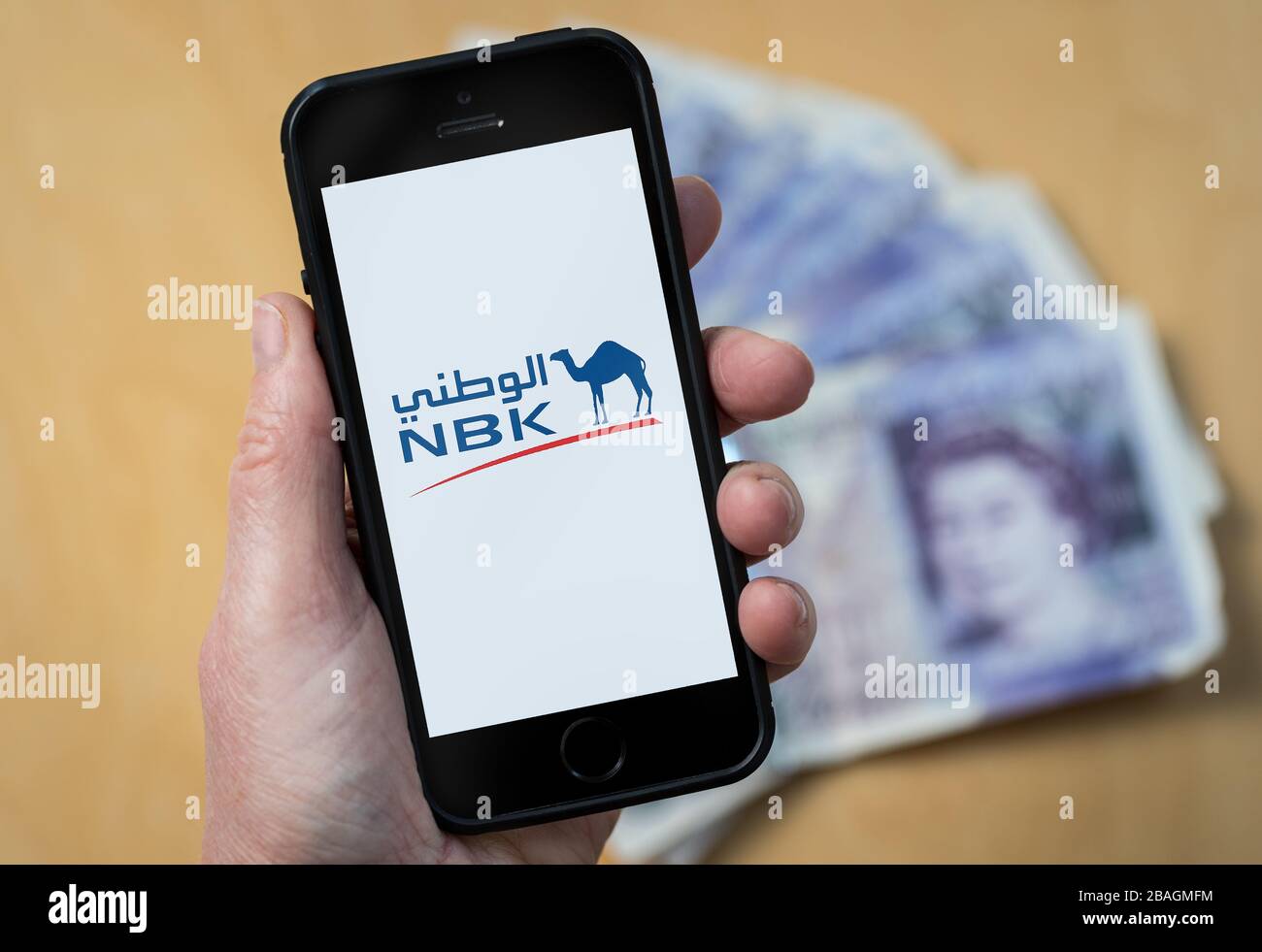 Une femme regardant le logo de la banque nationale du Koweït NBK sur un téléphone portable. (Usage éditorial uniquement) Banque D'Images