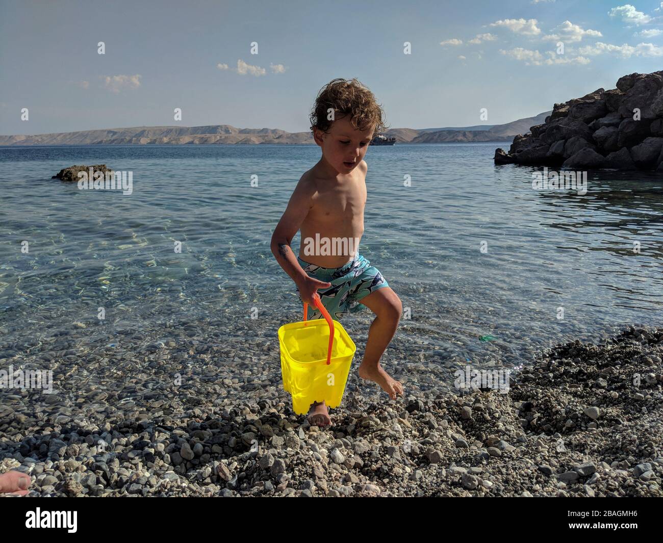 Petit garçon portant un pâle d'eau jaune soupir près de la mer Banque D'Images