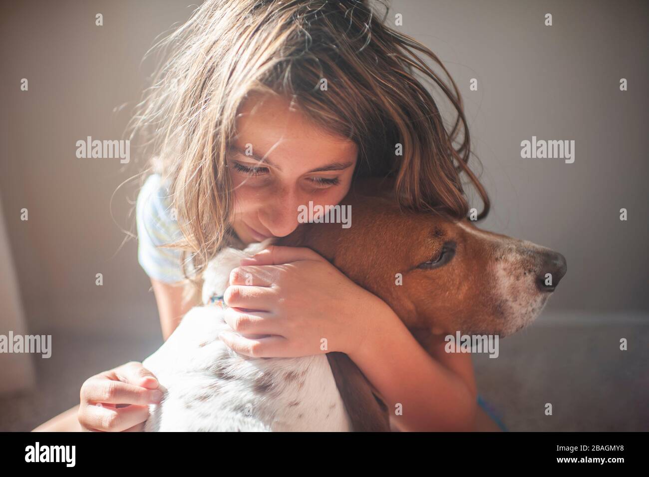 Happy Tween Girl embrassant son chien de chien de chien de race Basset à l'intérieur près d'une fenêtre Banque D'Images