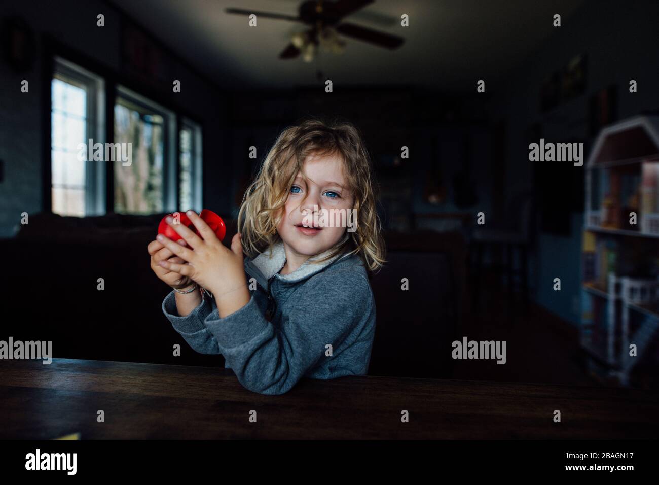 Jeune garçon aux cheveux longs blonds et aux yeux bleus assis à une table Banque D'Images