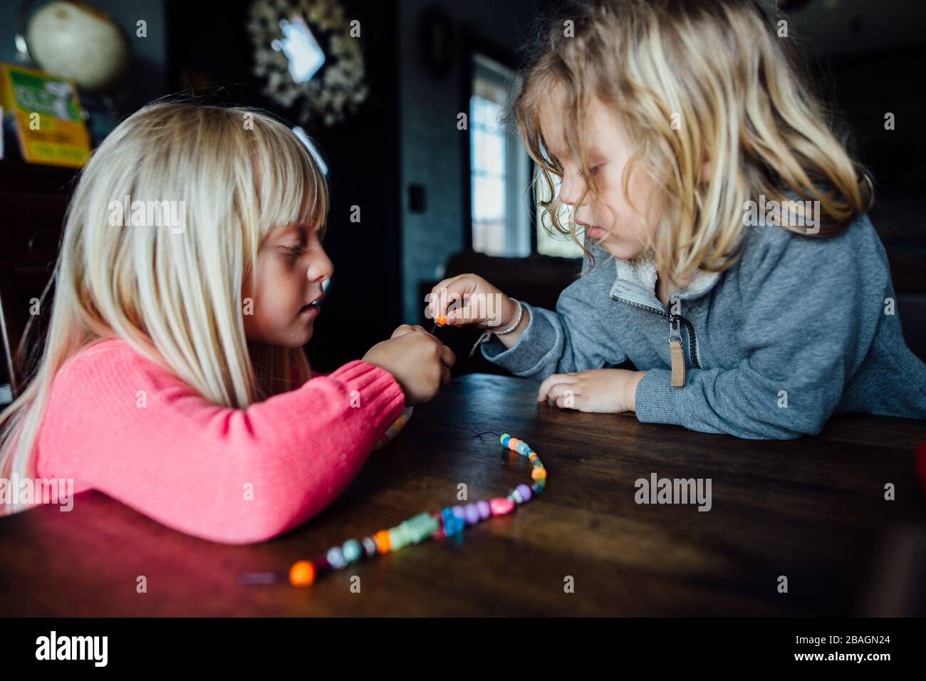 Petit garçon et fille faisant collier de perles à la table pendant la journée Banque D'Images