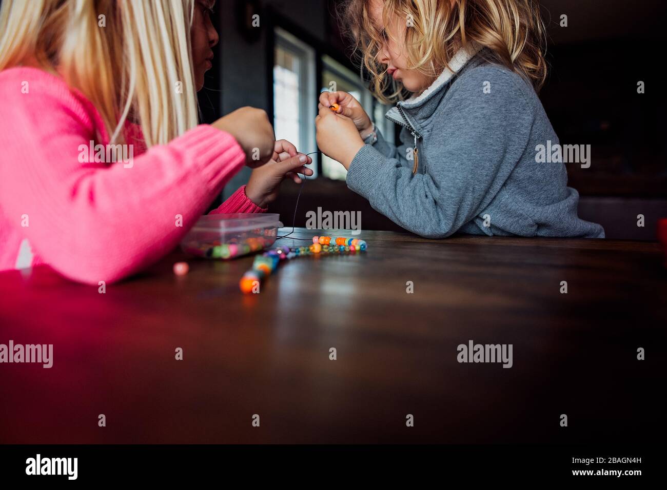 Petit garçon et fille faisant collier de perles à l'intérieur d'une table Banque D'Images