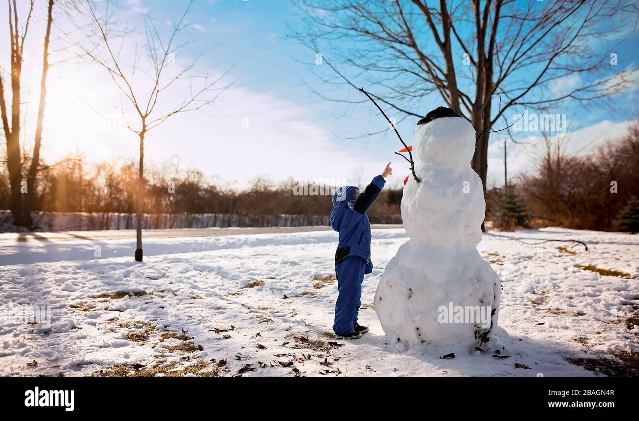 Petit garçon pointant vers un bonhomme de neige par beau temps Banque D'Images