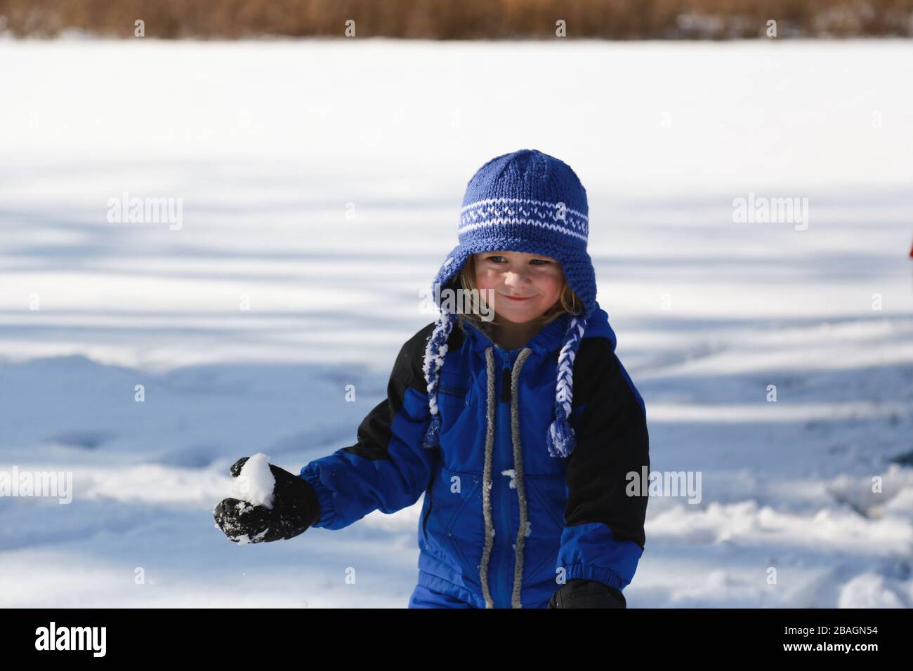Petit garçon tenant le ballon de neige dehors dans un manteau de neige bleu Banque D'Images