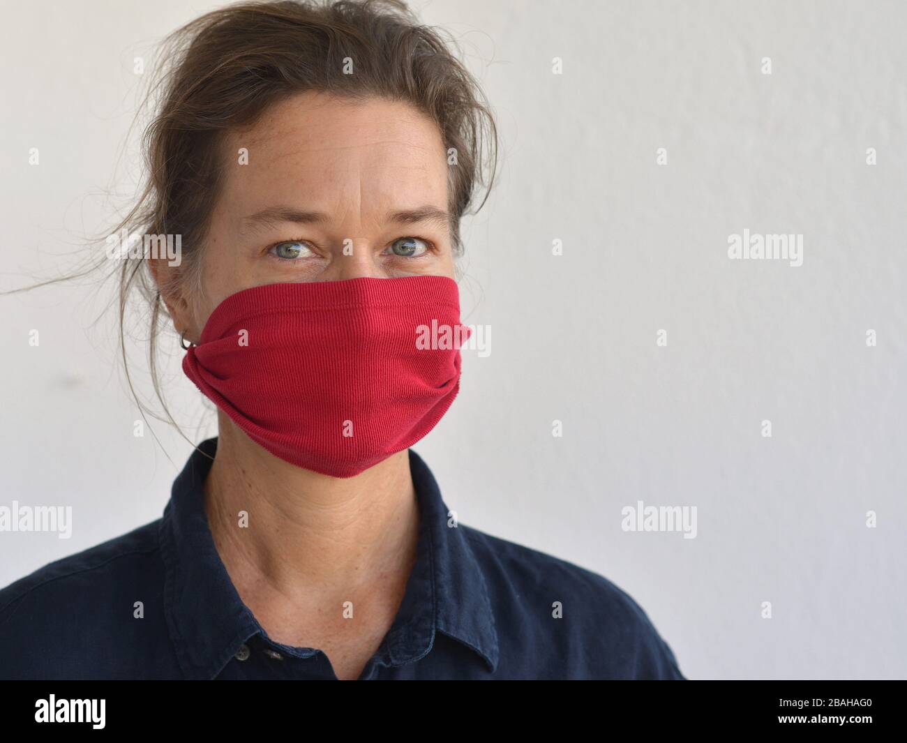 Femme caucasienne pose pour l'appareil photo avec son masque de visage de bricolage (fabriqué à partir d'une vieille pochette de t-shirt) pendant la pandémie de corona-virus 2019/20. Banque D'Images