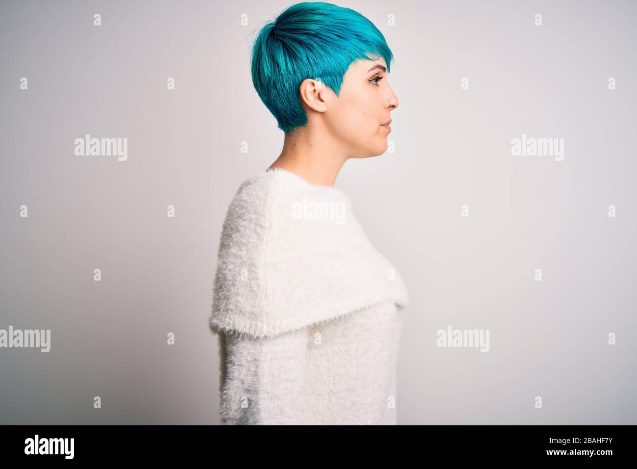 Jeune femme belle avec des cheveux de mode bleu portant un pull décontracté sur fond blanc regardant sur le côté, se détendre profil pose avec le visage naturel avec c Banque D'Images