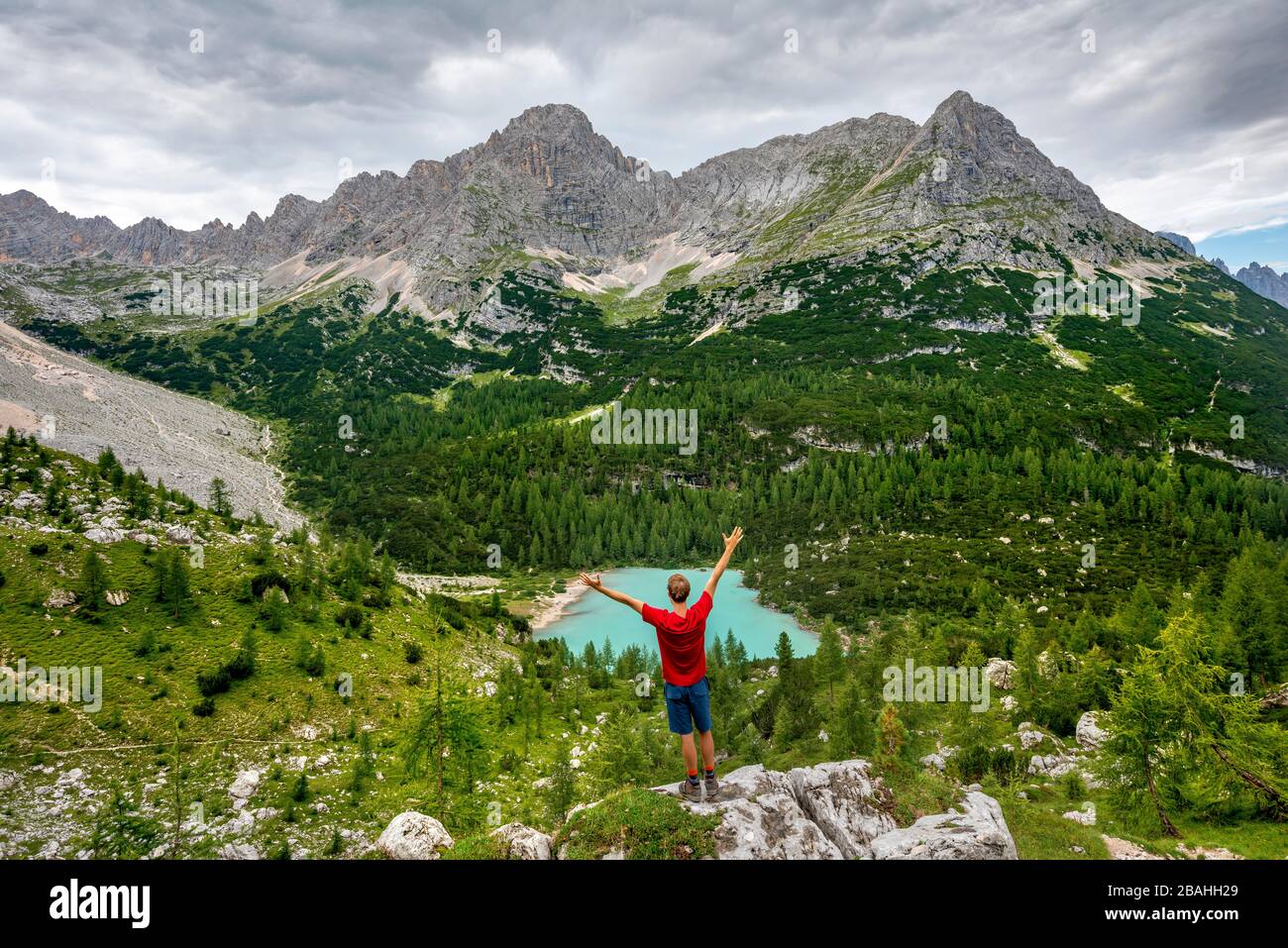 Jeune homme s'étire les bras dans l'air, randonneur se dresse sur les rochers et regarde le lac turquoise de Sorapiss et le paysage de montagne, Dolomites, Belluno Banque D'Images