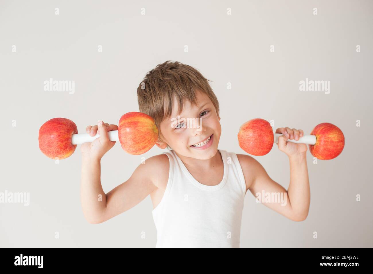 accueil à l'intérieur activité de loisirs de jeune petit enfant dans réservoir blanc haut levage haltères faits de pommes rouges pendant l'entraînement sportif Banque D'Images